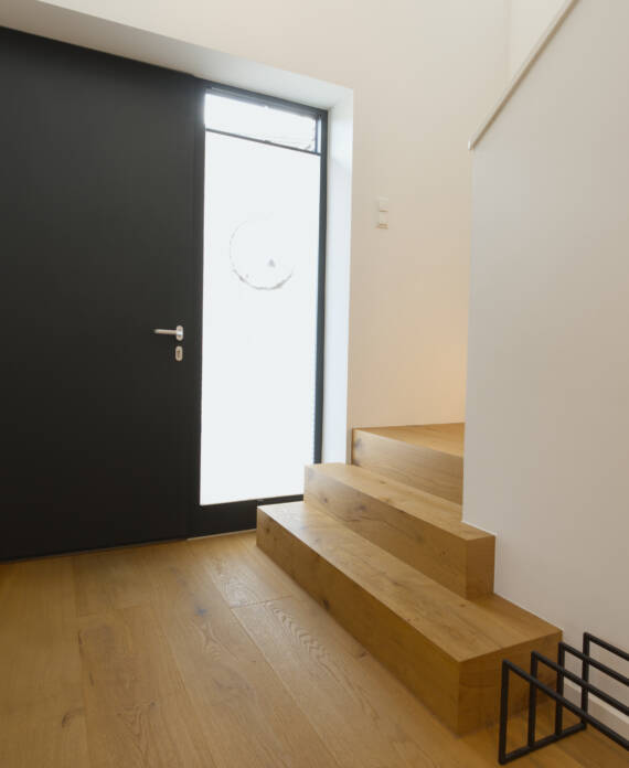 Eingangsbereich mit schwarzer Haustür und Holztreppe
