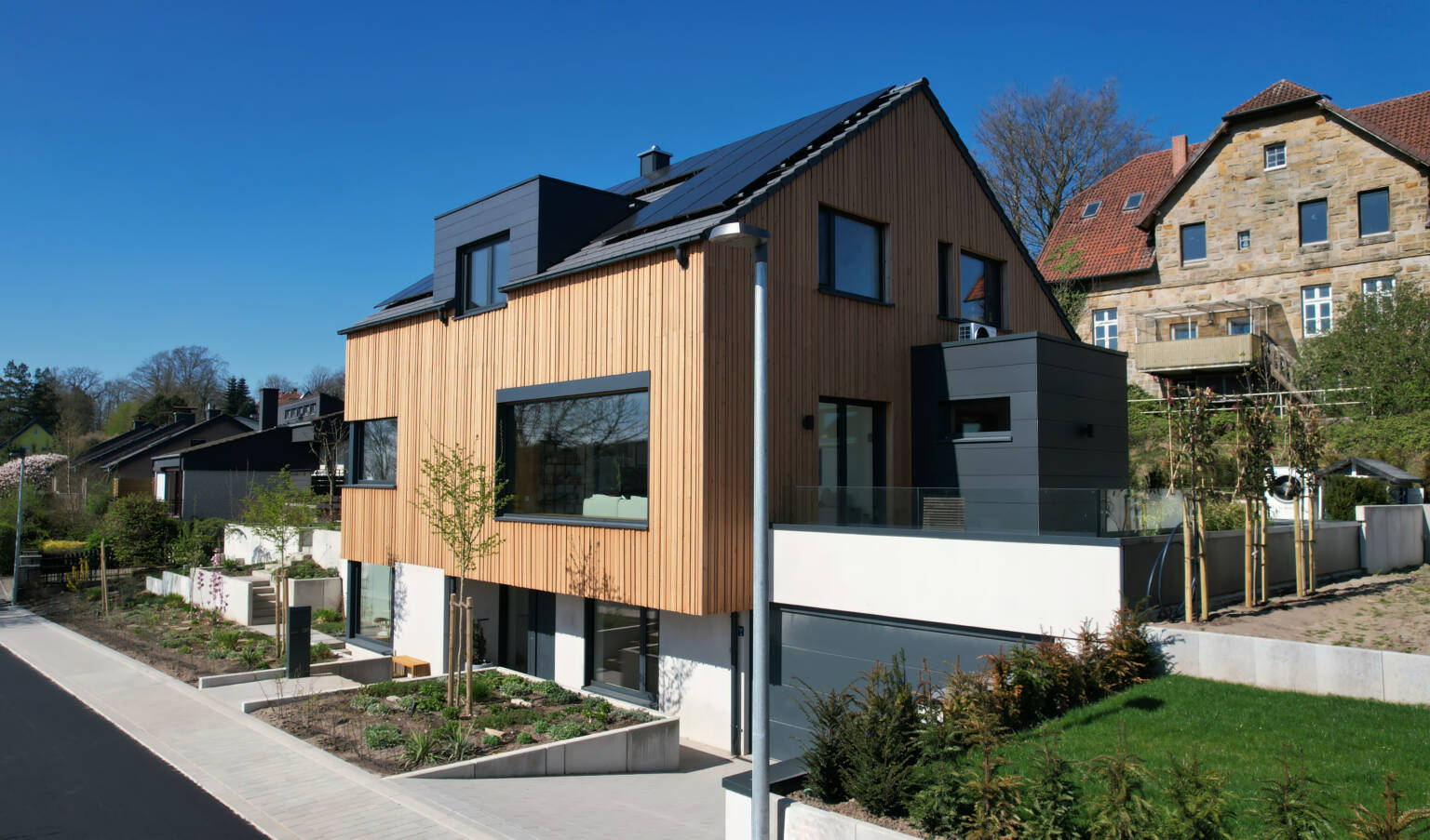 Massivhaus mit Holzfassade und großen Fenstern in Hanglage