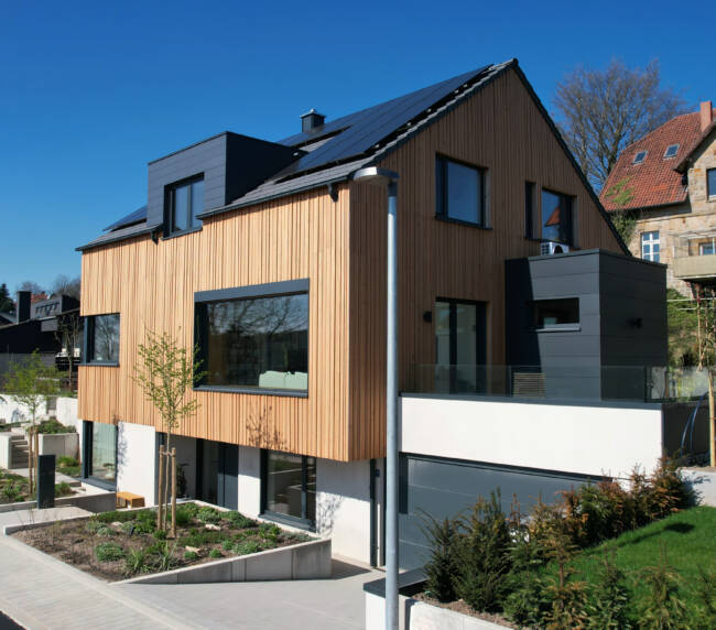 Massivhaus mit Holzfassade und großen Fenstern in Hanglage