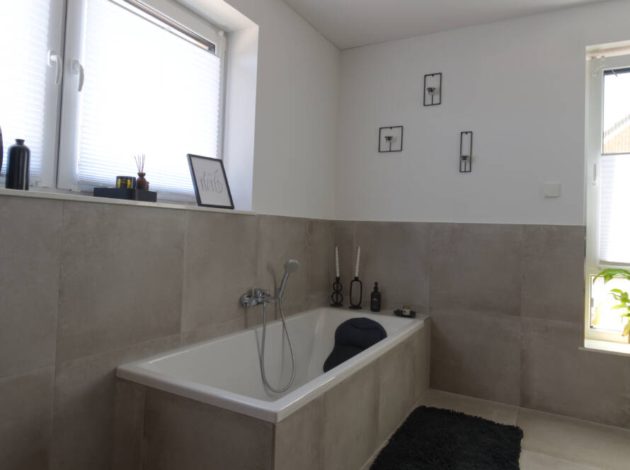 Halbhoch gefliestes Badezimmer mit Badewanne und schwarzen Deko-Elementen