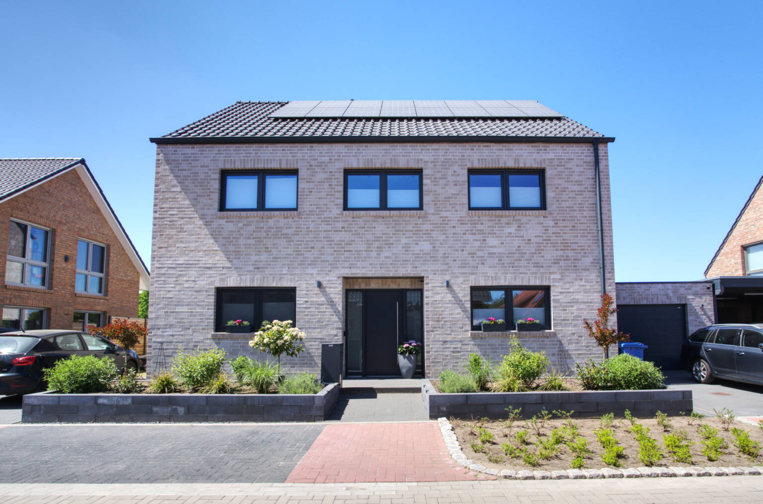 Modernes Massivhaus mit beige/grauem Klinker und dunklen Fenstern - Strassenansicht