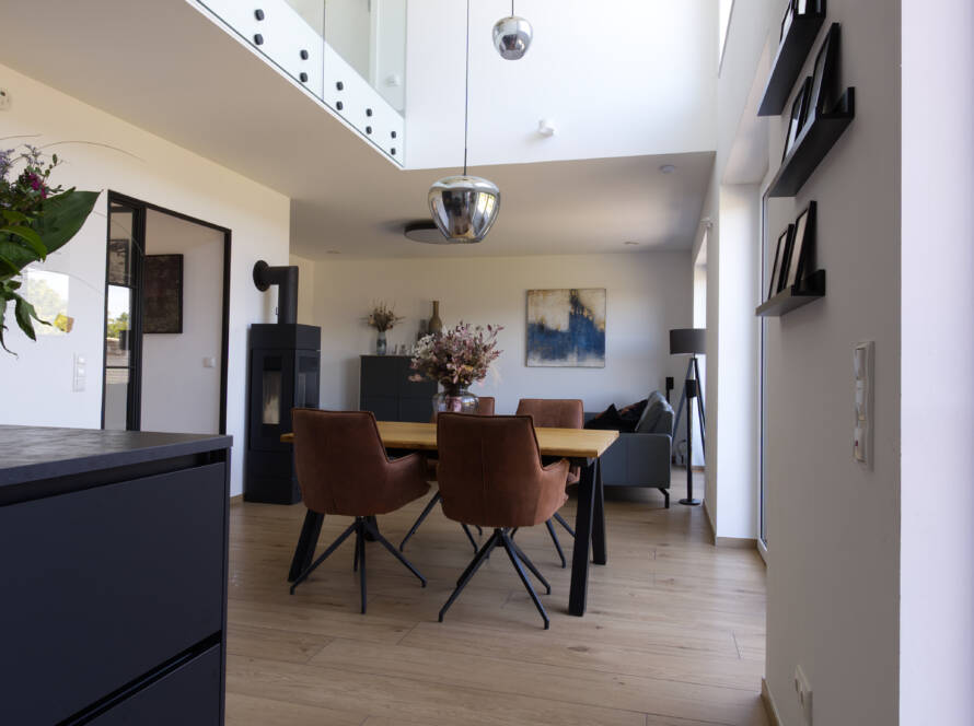 Blick von der schwarzen Küche aus in einen modernen Wohn- und Essbereich mit offener Galerie