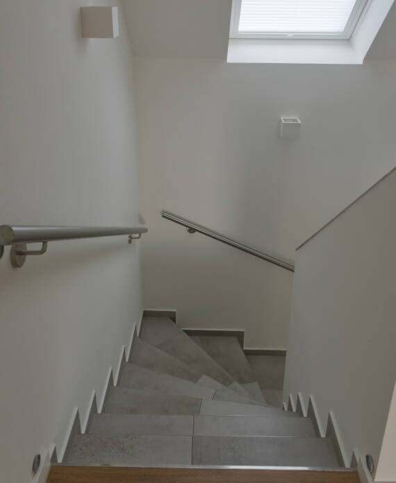 Halbgewendelte U-Treppe, grau gefliest mit Edelstahl Handlauf