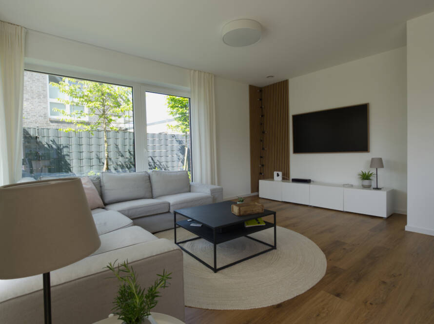 Wohnzimmer mit hellem Ecksofa, schwarzen Deko-Elementen und Fernseher an der Wand