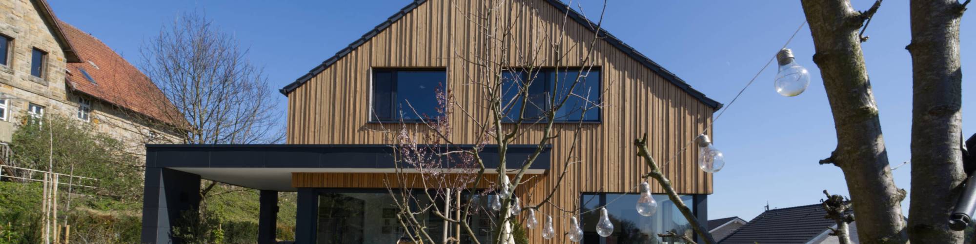 Massivhaus mit Holzfassade und überdachtem Terrassen-Bereich