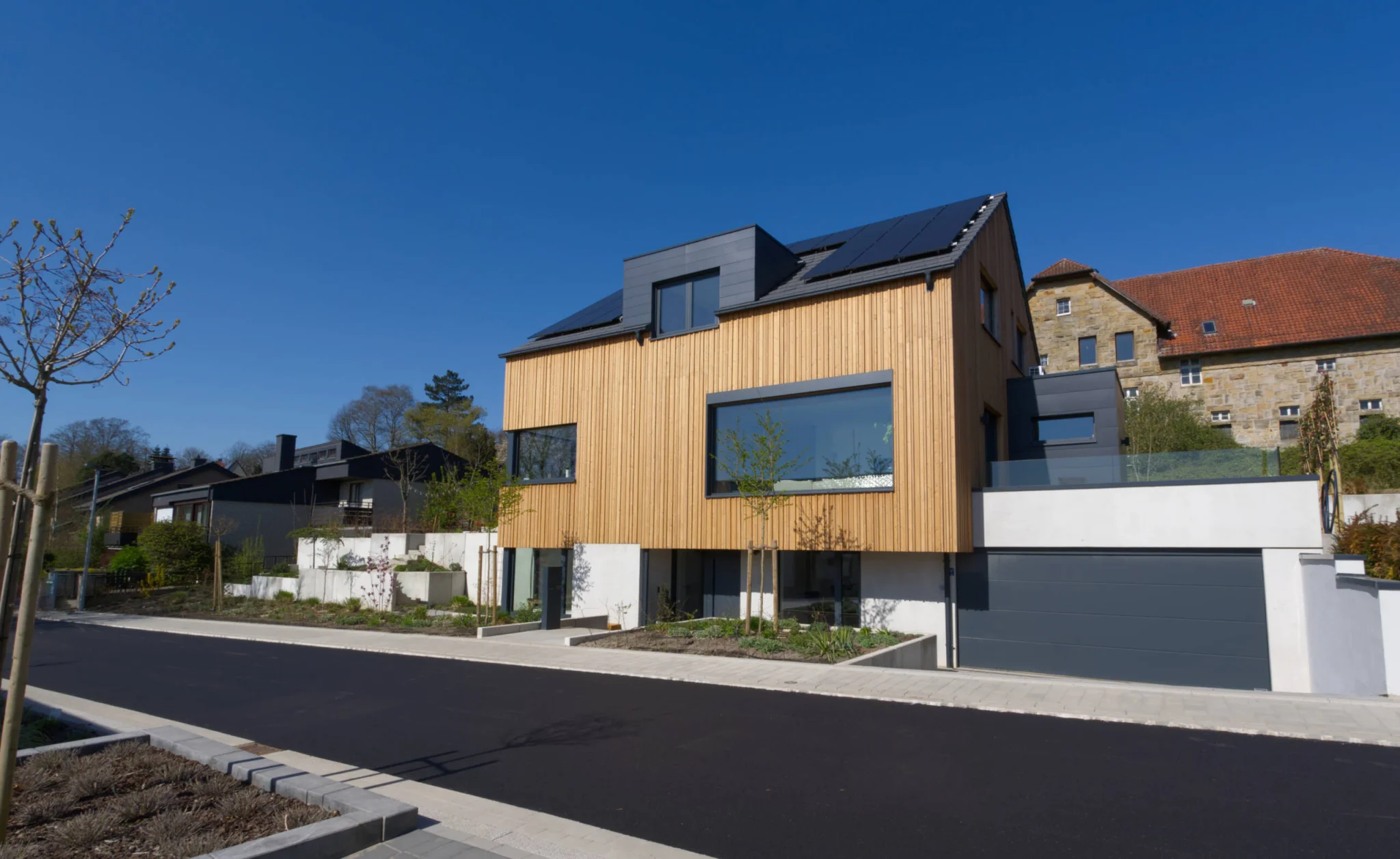 Massivhaus mit Holzfassade und großen Fenstern und Doppelgarage